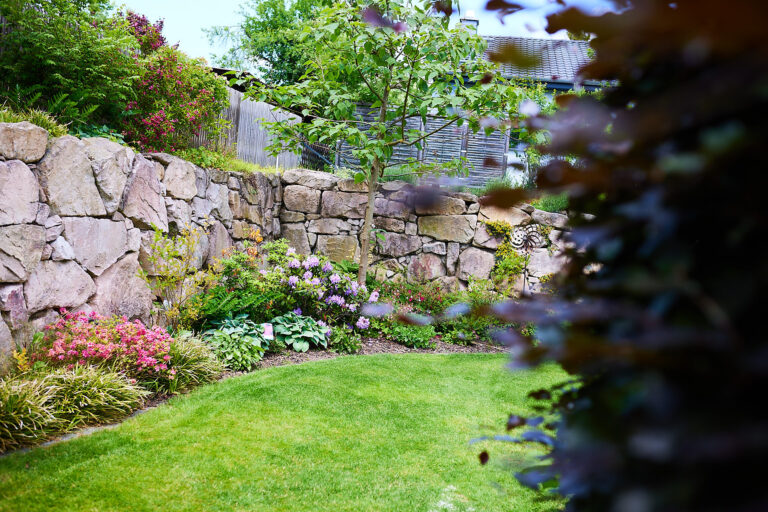 Mauer aus Naturstein und bunte Pflanzungen davor