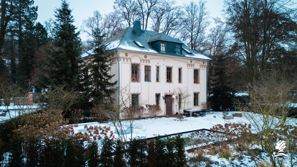 verschneiter Garten mir einem beigen großen Haus auf dem Grundstück