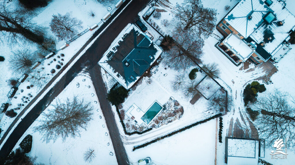 Drohnenaufnahme eines verschneiten Gartens mit Naturpool