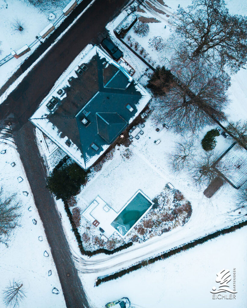 Drohnenaufnahme eines verschneiten Gartens mit Naturpool