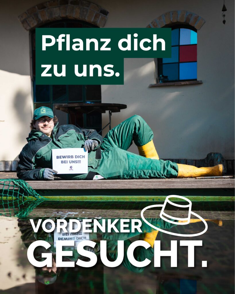 Eichler Mitarbeiter liegt in grüner Arbeitskleidung auf einer Terasse und hält ein Schild in der Hand mit der Aufschrift "Bewirb dich jetzt"