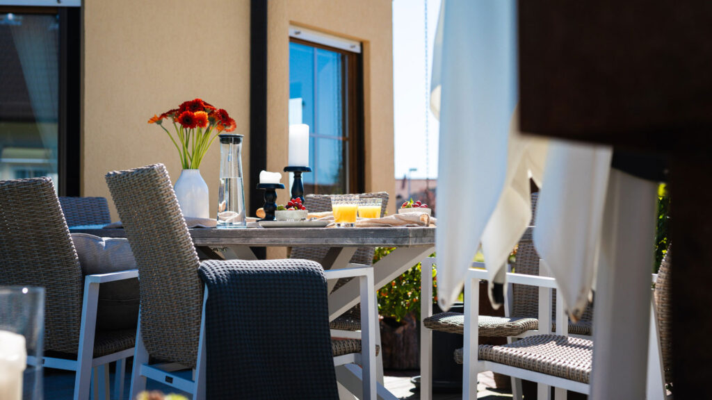 Ein modern gedeckter Holztisch auf einer Terrasse mit Blumen, Getränken und Kerzen