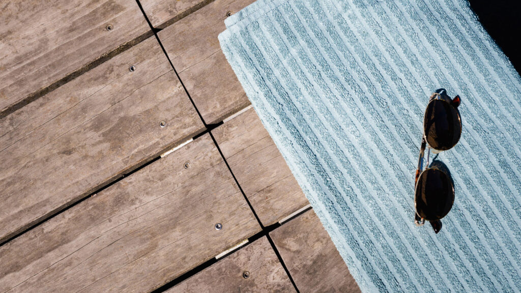 Eine Sonnenbrille liegt auf einem blauen Handtuch auf einer Holzterrasse