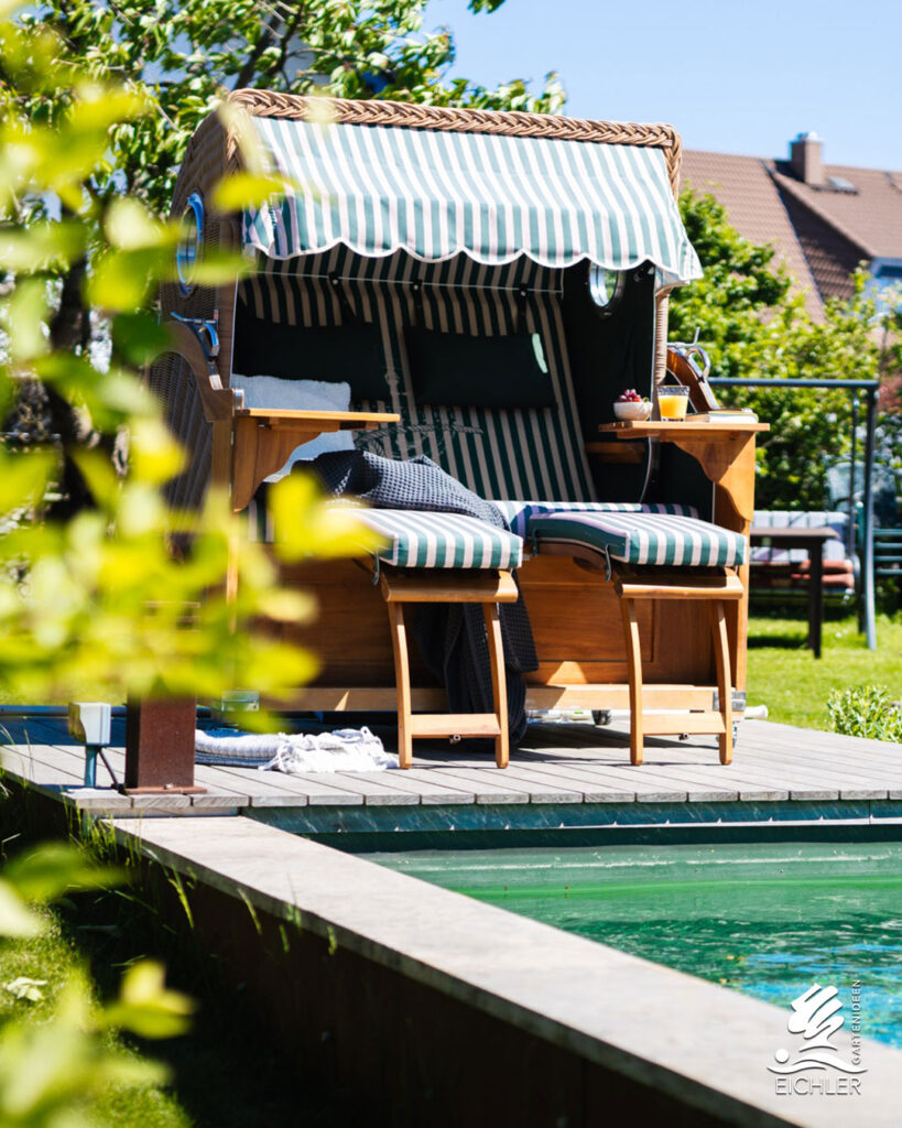 Perspektive durch Bäume auf einen Poolbereich mit Strandkorb und Holzstegen