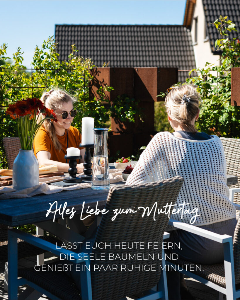 Zwei Frauen sitzen an einem Tisch im Garten und Frühstücken. Aufschrift: Alles Liebe zum Männertag