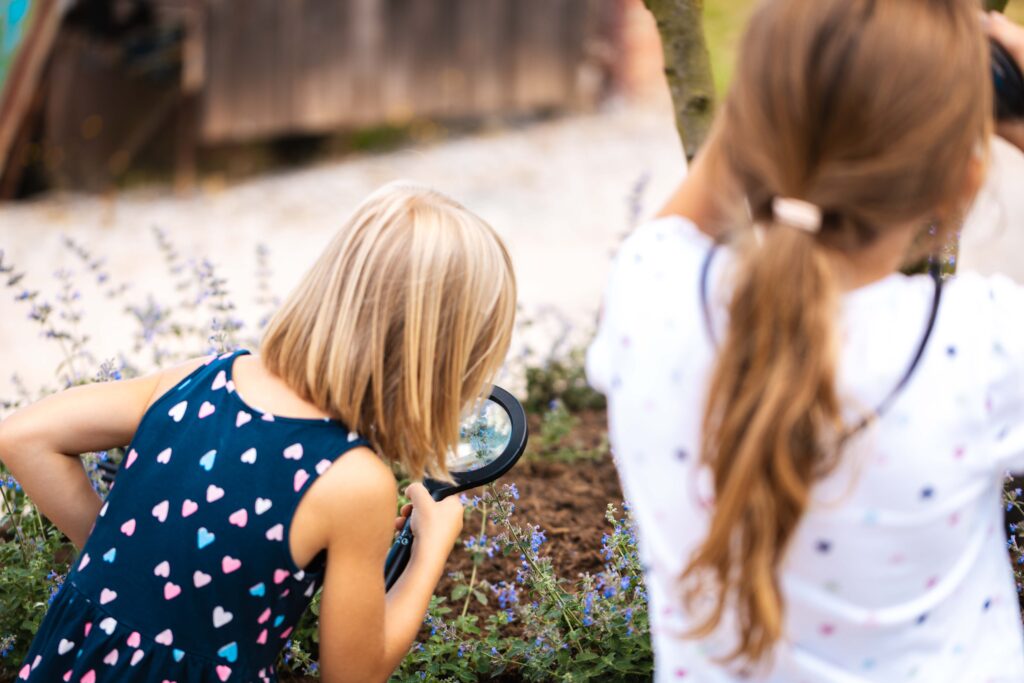 Zwei Mädchen erkunden Garten eine mit einer Lupe und eine andere mit dem Fernglas