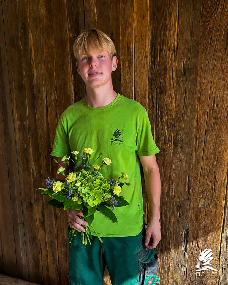 Azubi Nico hält nach bestandener Abschlussprüfung einen Strauß Blumen in der Hand
