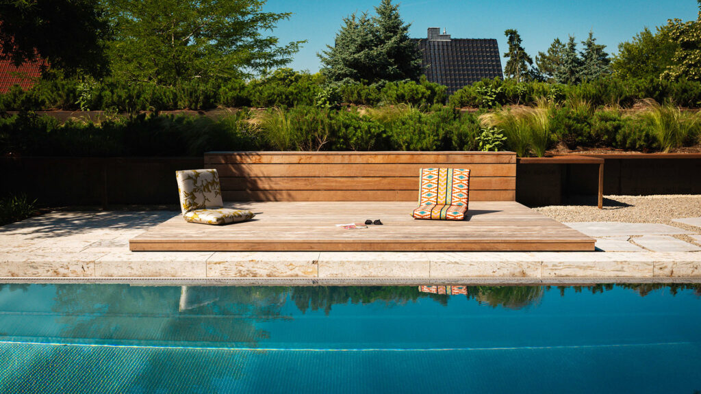 Moderne Outdoor-Sitzkissen auf einem Holzdeck direkt an einem Swimmingpool.
