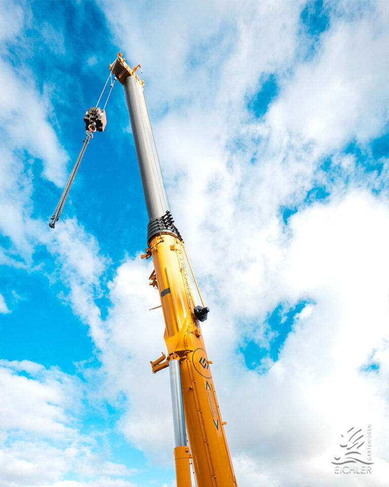 Der ausgefahrene gelbe Teleskoparm eines Mobilkrans ragt vor einem leicht bewölkten, blauen Himmel empor.